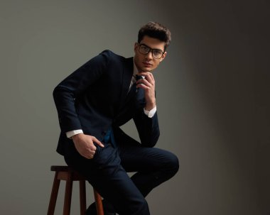 Düşünceli iş adamı, gri arka planda tahta koltukta otururken öne eğiliyor.