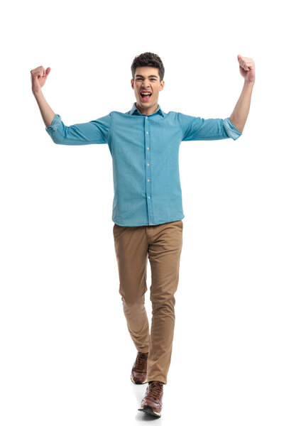 excited casual man celebrating with fists in the air while walking forward on white background