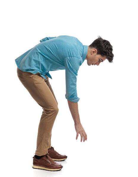 side view of casual man picking something up while standing on white background looking down