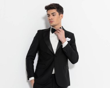 Siyah smokinli zarif bir sağdıcın portresi. Gri arka planda el ele tutuşup papyon takıyor.