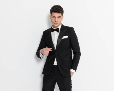 Siyah smokinli zarif damadın portresi. El ele tutuşup gri arka planda havalı olmak. 