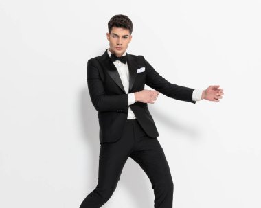 Siyah smokinli zarif genç damat gri arka planda poz veriyor. 