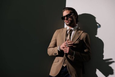 Kahverengi takım elbiseli çekici bir adam gri duvarın önünde yatarken yüzünü çeviriyor ve yüzükleri ayarlıyor.