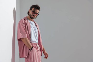 Güneş gözlüklü, gri arka planda el ele poz veren seksi bir adamın yan görüntüsü.