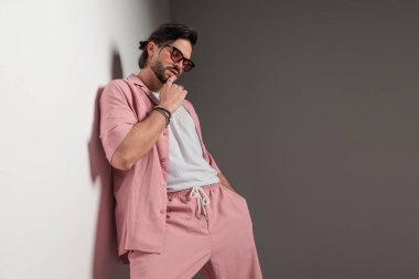 Güneş gözlüklü, dudaklarına dokunan ve stüdyoda duvara uzanmış el ele tutuşan şehvetli moda adamının portresi.