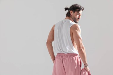 Arka planda, formda bir adamın kol kaslarını gösterirken ve bir elinde gri arka planda ceketi tutarken yan baktığı bir resim var.