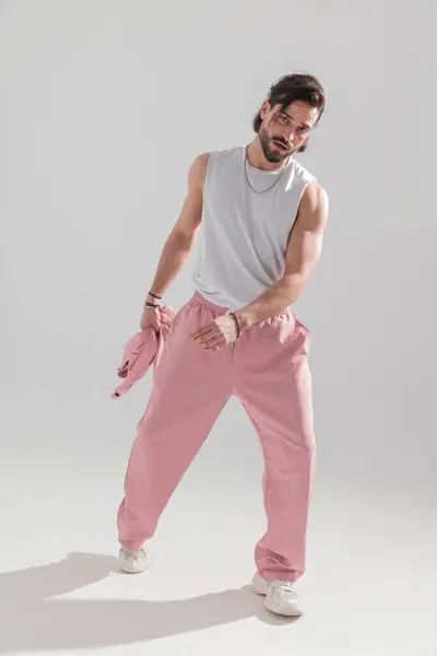 Stock image fit muscle man with beard holding jacket and posing in a cool way in front of grey background