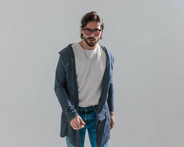 Güneş gözlüklü, kapüşonlu ve gri arka planda yürüyen çekici bir adamın portresi.