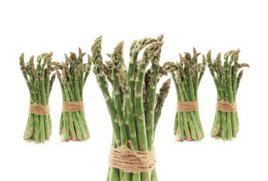 Stüdyoda beyaz arka planda iple bağlanırken 5 paket taze yeşil kuşkonmaz sebzesi ayakta duruyor.