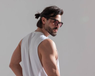 Uzun saçlı, güneş gözlüklü, beyaz tişörtlü, kaslı ve gri arka planda poz veren havalı adamın arka planı.