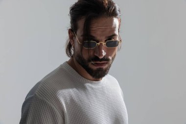 Dikdörtgen güneş gözlüklü havalı sakallı sıradan bir adamın gri arka planda kameraya bakarken çekilmiş bir fotoğrafını çek.