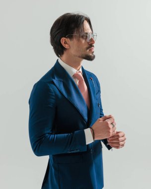 Çift göğüslü donanma takım elbiseli ve gri arka planda dikilirken yana bakan seksi erkek modelin yan görüntüsü