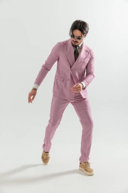 Çift göğüslü pembe takım elbiseli havalı manken aşağı bakıyor, kollarını moda pozunda tutuyor ve stüdyoda gri arka planda hareket ediyor.