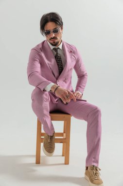 Stüdyoda gri arka planda otururken dirseğinde dirseğiyle poz veren kendine güvenen bir manken.