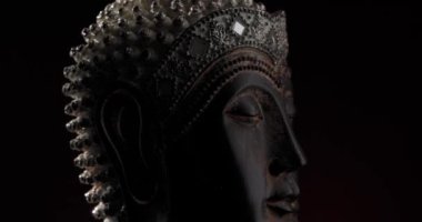 Dönen Buda heykeli, zarif bir taç ile karanlık arka planda dönerken iç huzur ve zihin meditasyonu kavramını gözler önüne seriyor.