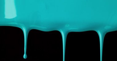 Mavi sıvı boya yavaşça aşağı akıyor ve siyah desenli bir yüzeye damlıyor, canlı ve soyut bir sahne yaratıyor.