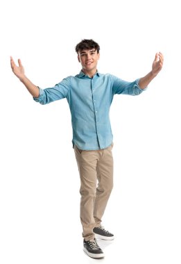 Kot pantolon giyen seksi bir genç adam, kollarını açıyor ve beyaz arka planda dururken sıcak bir gülümsemeyle karşılıyor.