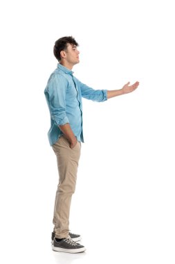 Bir eliyle ceplerini doldurmuş, elini kaldırmış ve kuyruğun neden hareket etmediğini merak eden genç adamın yan görüntüsü. 