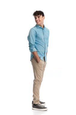 Arkaya bakan, kuyrukta bekleyen, elleri ceplerinde beyaz arka planda bekleyen mutlu nedensel adamın yan görüntüsü