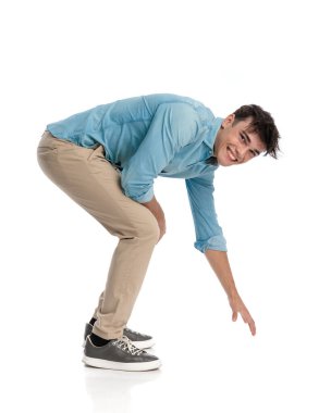 Heyecanlı genç bir öğrenci elini uzatıyor ve yerden bir nesne almak için, beyaz arka planda mutlu ve gülümsüyor.