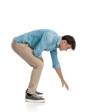 20 yaşında, mavi kot gömlekli çekici bir öğrenci beyaz arka planda yerden bir şey kapıyor. 