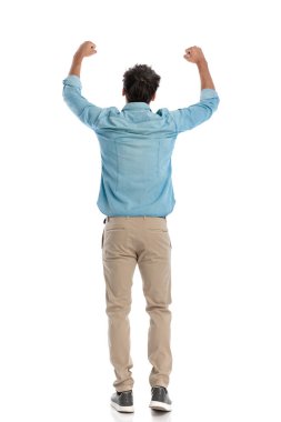 Arkadan görünen mavi kot gömlekli çekici genç bir öğrenci beyaz arkaplan önünde zafer kutlamaları yapıyor.