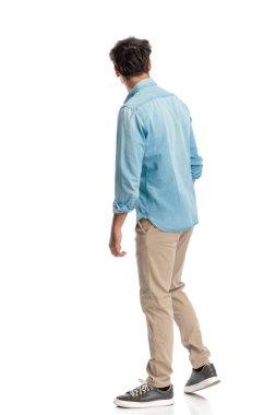 Mavi kot ve chino pantolonlu sıradan genç öğrencilerin stüdyoda beyaz arka planda yürümeleri ve bakmaları.