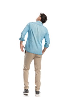 Gökyüzüne bakıp beyaz arka planda dikilirken uçak arayan sıradan kot gömlekli genç adam manzarasının arkasında.