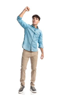 Yumruğu havada neşeli genç bir öğrenci beyaz arka planda dururken en sevdiği futbol takımının zaferini kutluyor.