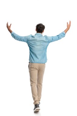 Arkadan görülen mavi gömlekli sıradan genç adam, kollarını gökyüzüne açıyor ve yürürken zafer ve minnettarlığını ifade ediyor.