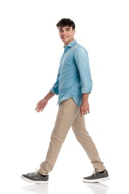 20 'li yaşlarda mutlu bir öğrenci. Gülümsüyor ve üniversiteye yürüyor. Beyaz arka planda kot bir gömlek giyiyor.