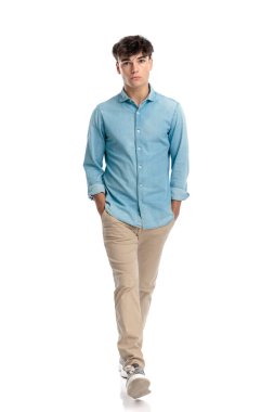 Mavi kot gömlekli sıradan bir genç kız ceplerinde el ele tutuşuyor ve beyaz arka planda hareket ediyor.