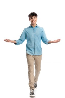 Mavi kot gömlekli yakışıklı genç adamın tüm vücudu beyaz arka planda yürürken kollarını açıp misafirleri selamlıyor.