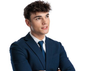 Mavi kravatlı mutlu bir öğrenci. Başka tarafa bakıyor, gülümsüyor, kollarını kavuşturuyor ve stüdyoda beyaz arka planda poz veriyor.