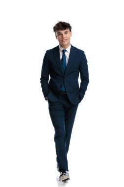 Lacivert takım elbiseli, kravatlı, elleri ceplerinde yürüyen ve beyaz arka planda gülümseyen genç iş adamları.