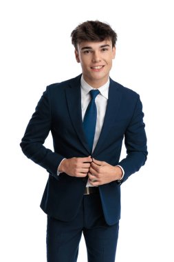 Yakışıklı işletme öğrencisi gülümsüyor ve lacivert takımını ilikliyor, ileriye bakıyor ve beyaz arkaplan önünde gülümsüyor.