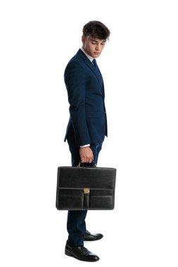 Yanında bavuluyla beyaz arka planda kuyrukta bekleyen genç bir işletme öğrencisi.