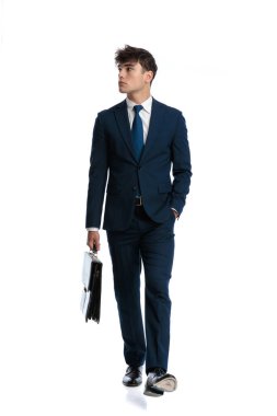 Mavili lacivert takım elbiseli havalı bir iş adamı bavulu tutuyor ve beyaz arka planda el ele yürüyor.