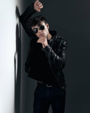 Şehvetli abd adam duvara yaslanıyor ve gri arka planda havalı bir adam gibi davranırken çenesine dokunuyor.