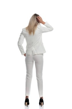 Beyaz takım elbiseli kafası karışık bir iş kadını beyaz arka plan önünde zor sorunları çözmenin yollarını düşünüyor.