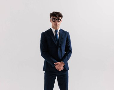 Lacivert takımlı, gözlüklü, el ele tutuşan ve gri arka planda poz veren seksi genç adam.