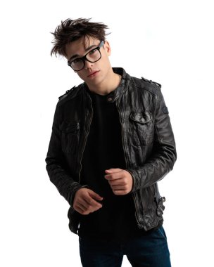 Gözlüklü, siyah deri ceketli ve beyaz arka planda kendine güvenen genç bir rockçı.