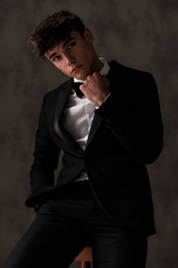 Siyah smokinli zarif bir gencin portresi papyon takıyor ve bej desenli arka planda el ele oturuyor.