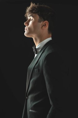 Siyah takım elbiseli yakışıklı genç adam elleri ceplerinde ve gözleri kapalı dikilirken