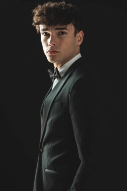 Siyah smokinli genç damadın siyah arka planda dikilirken ceplerini tutuşu.