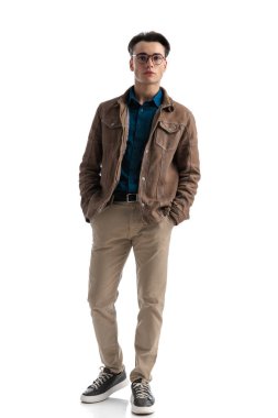 Beyaz arka planda duran, kahverengi deri ceket giymiş çekici, zeki, sıradan bir adam.