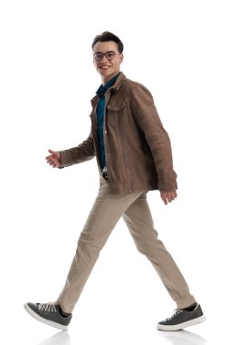 Kahverengi deri ceket ve gözlük takmış, yürüyen ve gülümseyen mutlu, sıradan bir adamın yan görüntüsü.