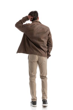 Kafası karışmış, beyaz arka planda dikilirken başını kaşıyan, tüm vücudunu gösteren bir adam.