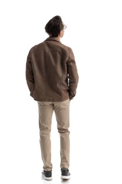 Beyaz arka planda elleri ceplerinde dikilirken yan yana bakan akıllı sıradan bir adamın arkasında.