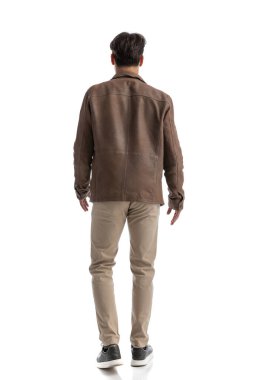 Kot pantolon ve kahverengi deri ceket giymiş genç bir adamın arkasında beyaz arka plana basıyor, tüm vücudu resmediyor.